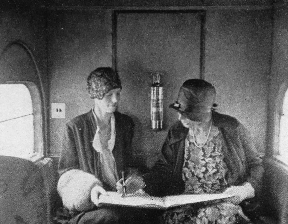 Photo close shot of Earhart and Mrs. Putman jointly holding a large book being while Putman signs it