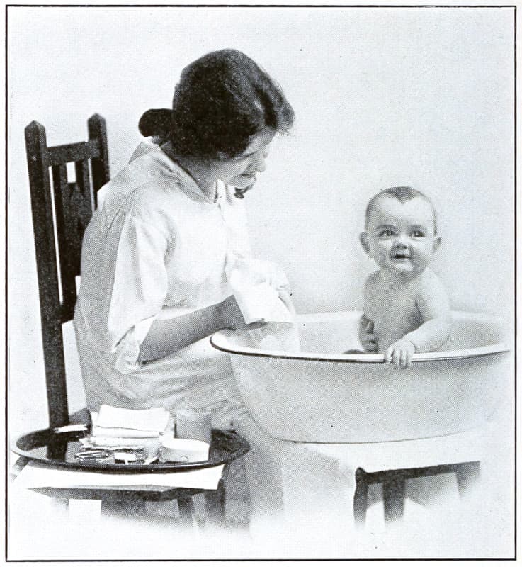 A girl bathing a baby in a small tub