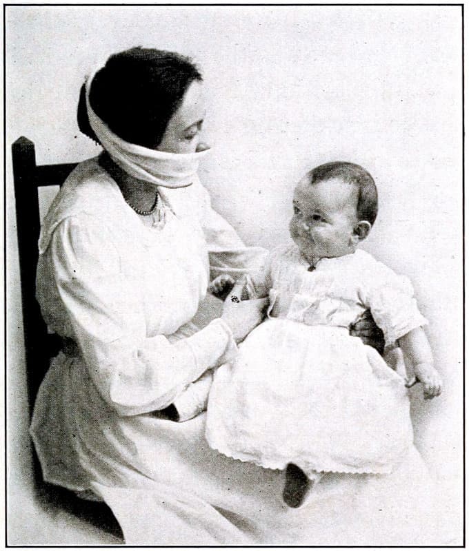 A woman wearing a mask covering their mouth and nose while holding a baby